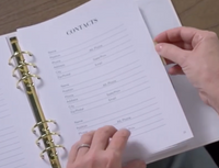 Close-up of My Health Journal white linen edition open to the Contacts page with fields for name, phone, address, and email